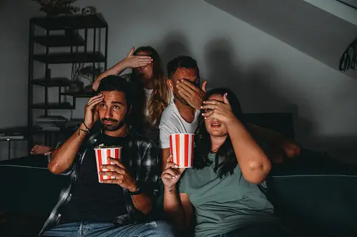A group of four friends are watching TV at home while they are eating popcorn haunted movies picture