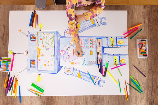 A young girl sits at her desk and drawing robot.