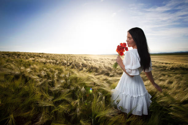 Lovely youg girl in a wheat field holding a poppy bouquet.