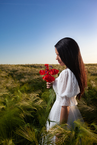 Young beautiful woman in a wheat field holding a poppy bouquet.