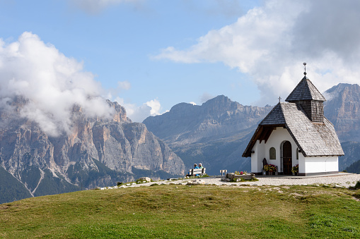 Old couple sitting on a bench near a little church looking to dolomites mountains