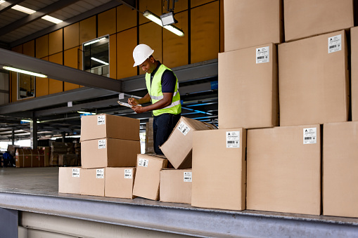 African American man working at a distribution warehouse and doing an inventory of the merchandise to be shipped - freight transportation concepts