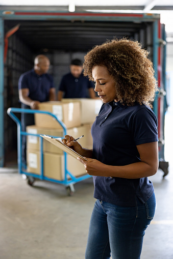 African American woman working at a commercial dock supervising the shipping of cargo  in trucks - freight transportation concepts