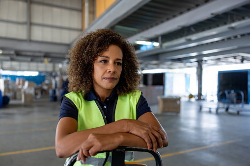 Portrait of an African American woman working at a distribution warehouse using a pallet jack - freight transportation concepts