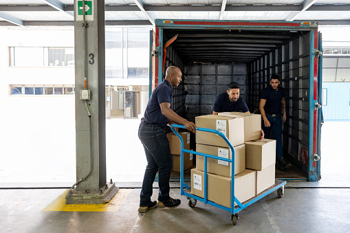 Group of workers using a pallet while loading merchandise on a truck at a distribution warehouse -freight transportation concepts