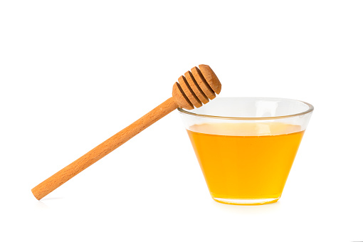 Fresh honey in a glass transparent bowl with a wooden dipper on a white isolated background. Honey in an open glass jar with a honey stick. Honey on a white background.