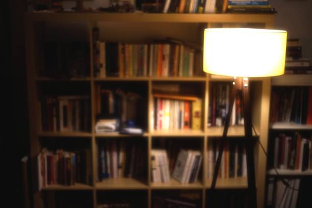 Glowing light bulb in mid-air over the blank books on a shelf against blue wall with copy space.