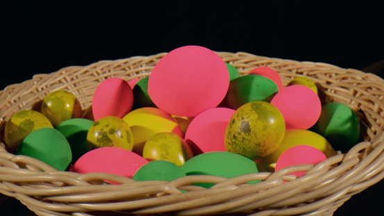 Multicolored green, pink, yellow Easter eggs in a wicker basket - black background & close up