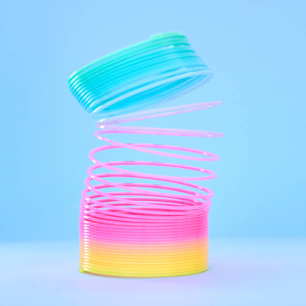 istock Rainbow slinky toy, spring and plastic product in studio isolated against a blue background mockup. Flexible toys, colorful spirals and childhood item stretched out for playing, having fun and games. 1471709296