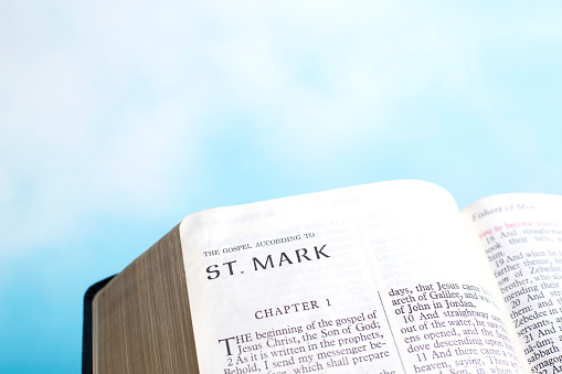 Bible open to the book of St. Mark.  Close up with beautiful soft heavenly sky in the background.