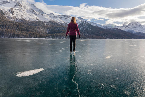 Subject: Horizontal view of a girl in a figure skating pose skating close to the cracks created by the freezing Engadin winter, Lake Silvaplana, canton of Grisons, Engadine, Switzerland