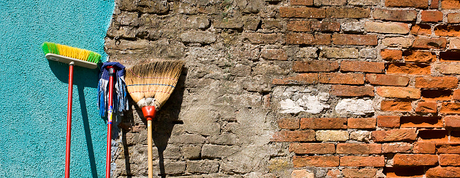 Mop and brooms leaning on old brick wall, copy space available on the right.