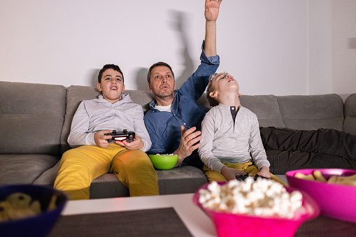 Caucasian family, father and sons having fun while playing video games on PlayStation