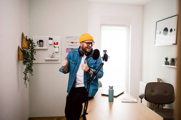 istock Young smiling man recording podcast and doing live streaming using microphone and headphones in recording studio 1471717986