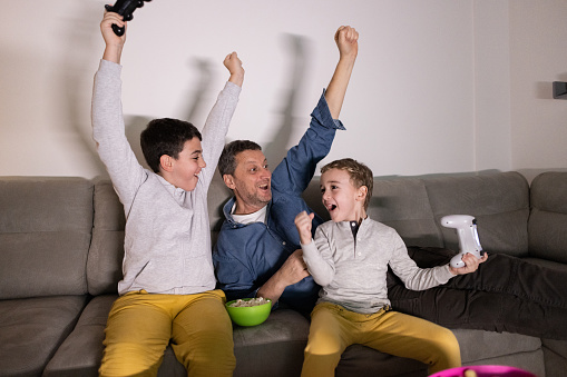 Caucasian family, father and sons having fun while playing video games on PlayStation