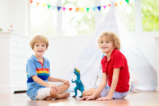 Kids room with teepee tent. Children play in white sunny bedroom. Cozy light interior for kid nursery or playroom. Little boy with toy blocks and dinosaur playing on wooden floor. Home decoration.