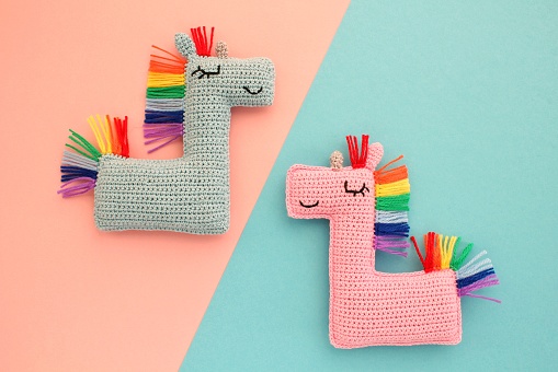 Crochet amigurumi handmade stuffed soft colored unicorn toys with rainbow mane on pink and blue background