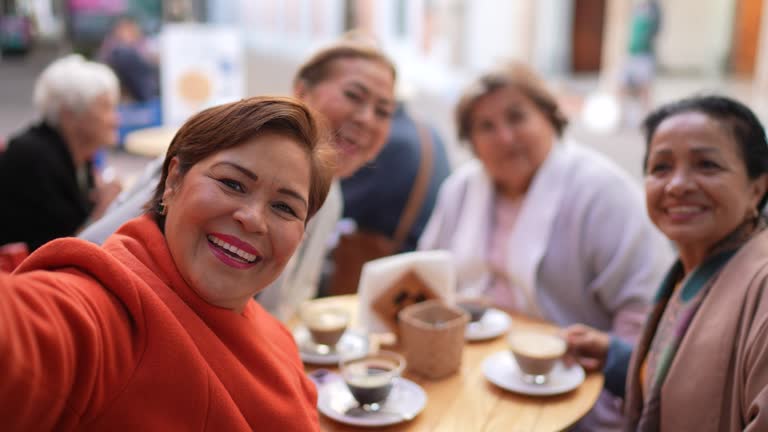 Senior friends taking a selfie at coffee shop outdoors - camera point of view