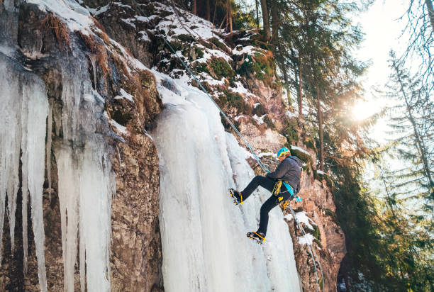 Ice climber dressed in warm winter climbing clothes, climbing harness and helmet abseiling frozen waterfall. Active people and sports activities concept image.