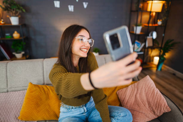 istock Smiling young woman taking selfies while relaxing in living room 1471725655