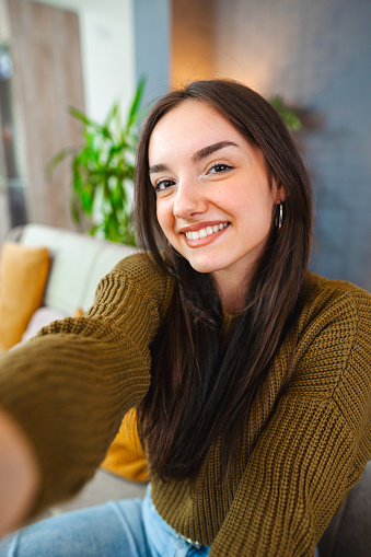 Smiling young woman taking selfies while relaxing at home