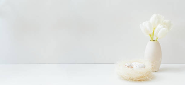 istock White spring tulips in a vase, easter eggs on a white table. Mock up for displaying works 1471726238
