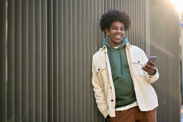 istock Happy young African American guy using phone standing at wooden wall. 1471727296