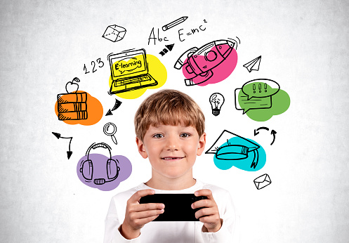 Smiling handsome boy in casual wear standing holding smartphone near concrete wall with education sketch. Concept of ambitious child, startup, young generation, school subjects, distant learning