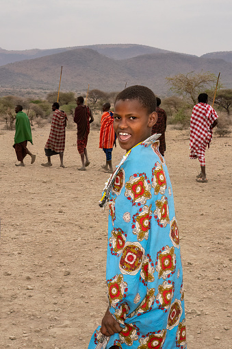 Karatu, Tanzania - October 16th, 2022: A young masai woman in a traditional outfit, dancing and singing with her tribesmen during a show for tourists near their village.