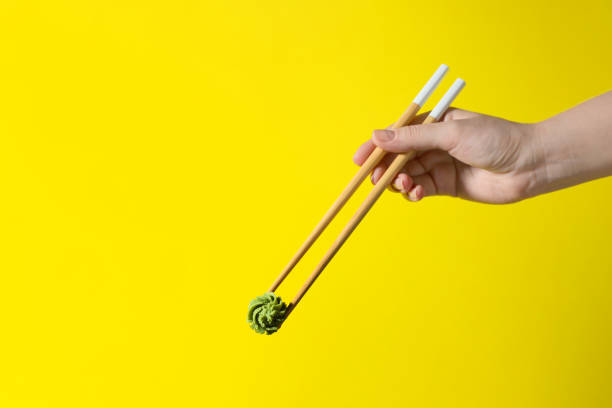 woman holding swirl of wasabi paste with chopsticks on yellow background, closeup. space for text - wasabi imagens e fotografias de stock