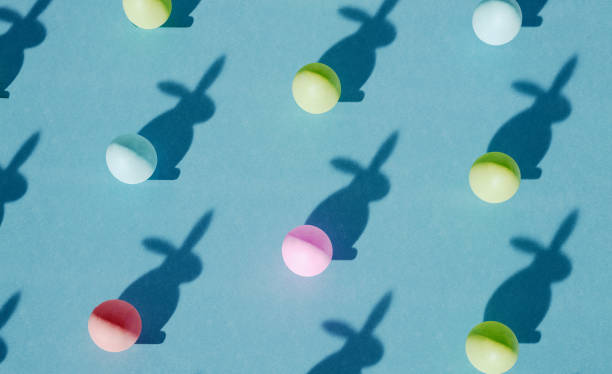 Isometric pattern made of colorful easter eggs with funny rabbit shadow on pastel blue cardboard. Spring concept for design templates or greeting card.