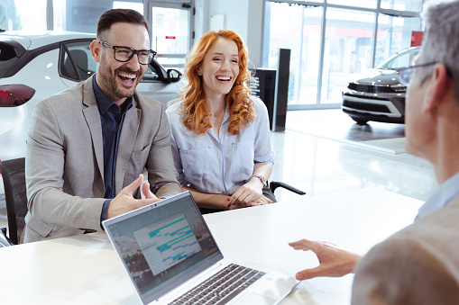 Happy couple and car salesperson talking in car dealership