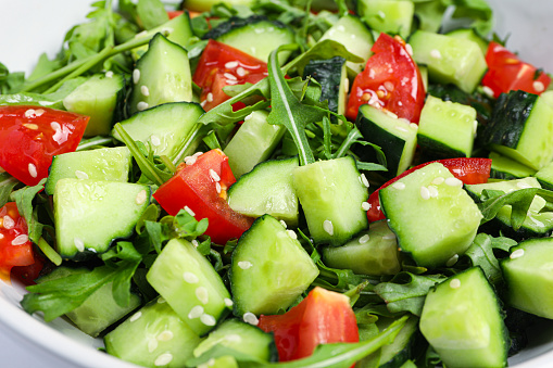 Delicious salad with cucumbers, tomatoes and sesame in bowl, closeup