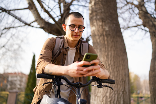 Young man using mobile phone with his bike, outdoors.