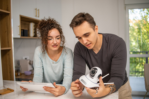 A young couple installs a security camera in their new home, an alarm system, they plan where best to install the video surveillance of their new apartmentv