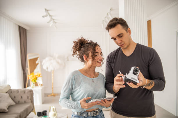 A young couple, a man and a woman, are setting up a security camera for home surveillance in their apartment stock photo
