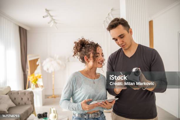 A Young Couple A Man And A Woman Are Setting Up A Security Camera For Home Surveillance In Their Apartment Stock Photo - Download Image Now