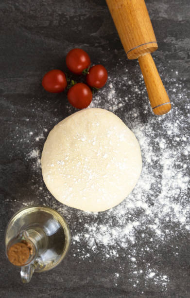 istock Background for making pizza, raw dough, cherry tomatoes, and a rolling pin for rolling out the dough on a dark background. Pizza cooking concept. 1471758634