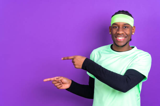 Black ethnic man in green clothes on a purple background, pointing at a free copy space