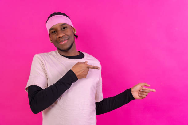Black ethnic man in pink clothes on a pink background, pointing to a free right copy space
