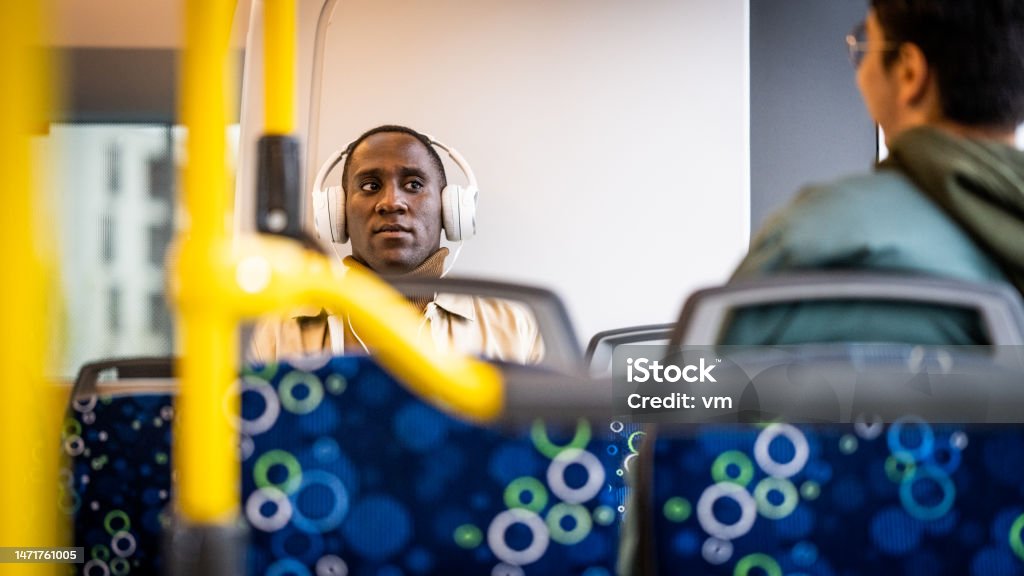 Man in headphones riding bus and talking with passenger African american young adult man in headphones riding public bus and talking with passenger 20-24 Years Stock Photo