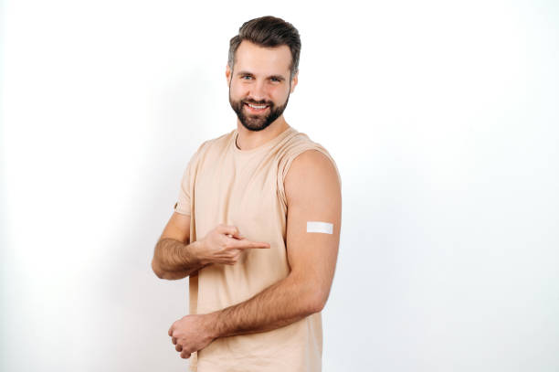 istock Happy caucasian man, with a plaster on his shoulder, received a vaccine, points a finger at it, stands on a white isolated background, looks at camera, smile. Vaccination, disease prevention 1471762833