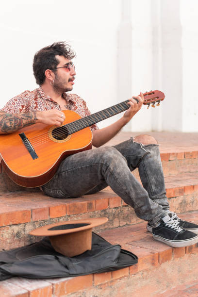 istock Young man sitting on the sidewalk playing guitar for money 1471764018