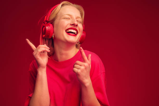 Una donna allegra che ride, balla e si gode la musica mentre è isolata su sfondo rosso. - foto stock