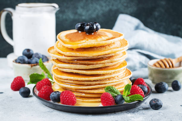 istock Delicious pancakes, with fresh blueberries, raspberry and maple syrup or honey on a dark background 1471773299