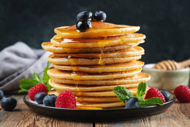 istock Delicious pancakes, with fresh blueberries, raspberry and maple syrup or honey on a dark background 1471773302