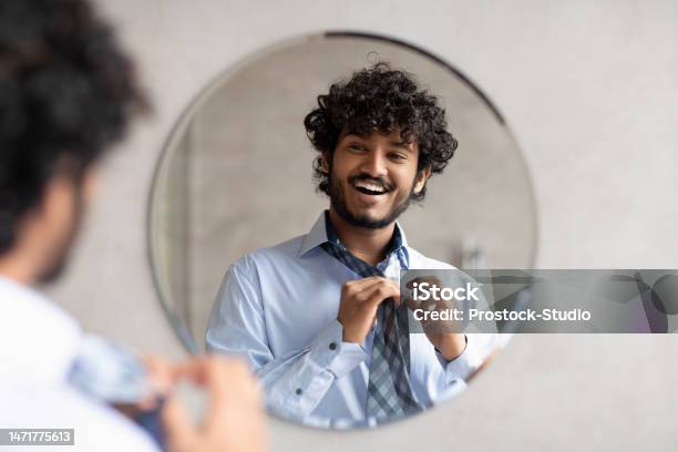 Happy Indian Businessman Putting On Necktie While Looking In The Mirror Standing In Modern Bathroom Free Space Stock Photo - Download Image Now