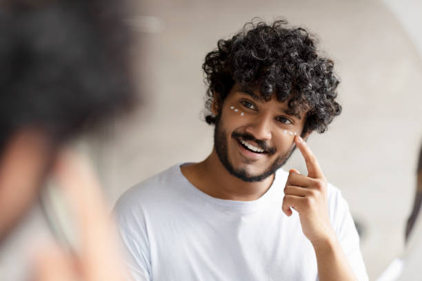 istock Indian man applying cream under her eyes and smiling at his reflection in mirror, enjoying morning beauty routine 1471775632