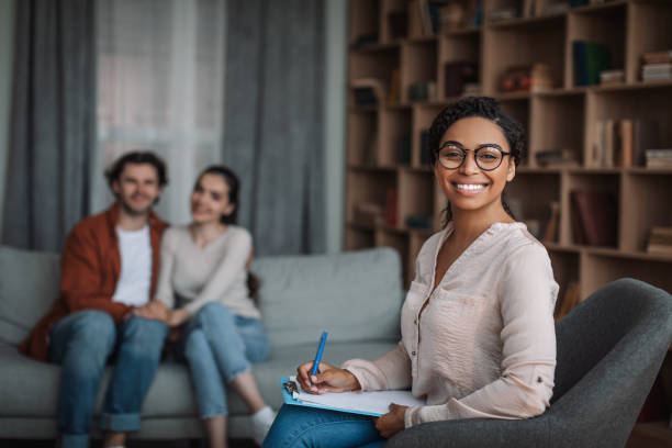 Smiling young european guy and lady sit on sofa at meeting african american woman doctor psychologist stock photo