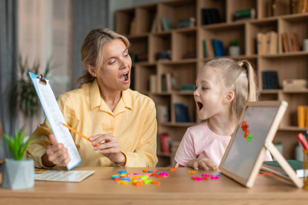 istock Speech training for kids. Professional specialist training with little girl, teaching her right articulation exercises 1471775730